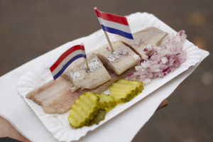Raw herring eaten with pickles, chopped onions, and a toothpick flag...